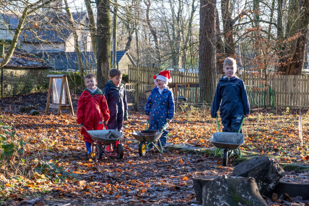 4 children outside with wheelbarrows amongst the fallen leaves