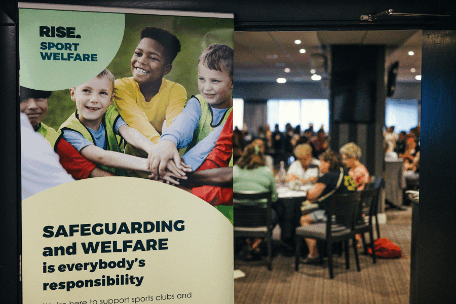 A Rise safeguarding and welfare banner, with attendees of the North East sport welfare event in the background
