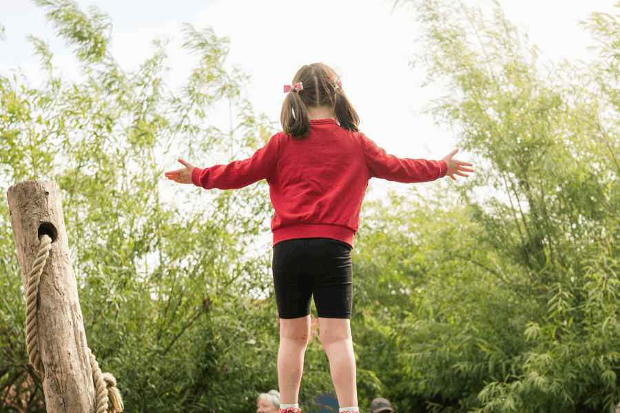Young girl outdoors stood with her back to the camera, facing the trees