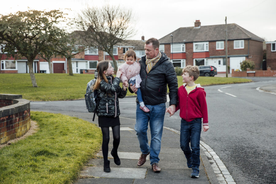 A father walking his children (a young boy, girl, and a toddler), to school.